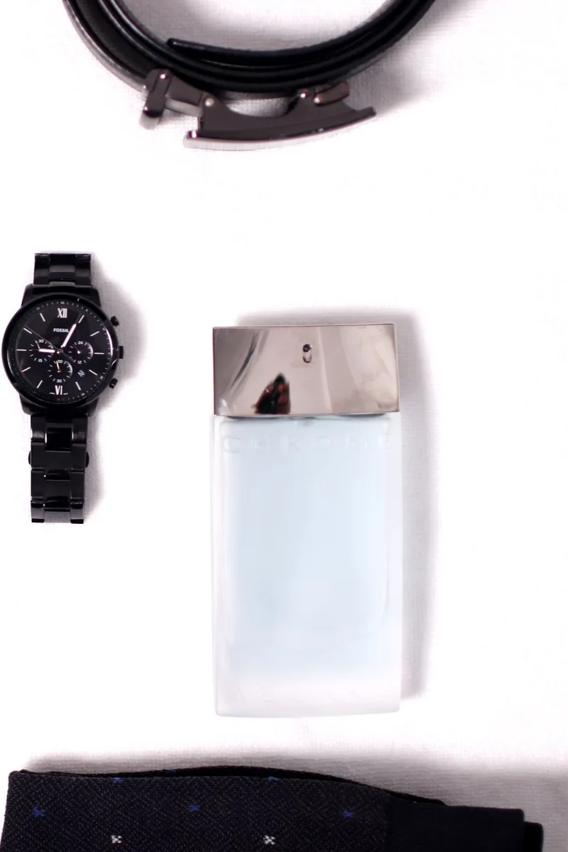 Reloj, corbata, cinturón y perfume dispuestos sobre fondo claro