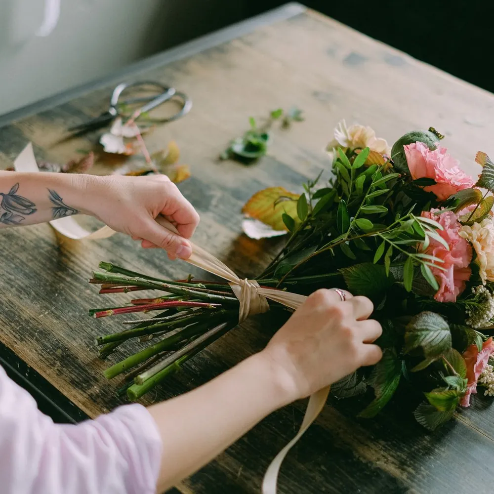 Manos arreglando un ramo de flores en tonos durazno sobre una mesa de madera