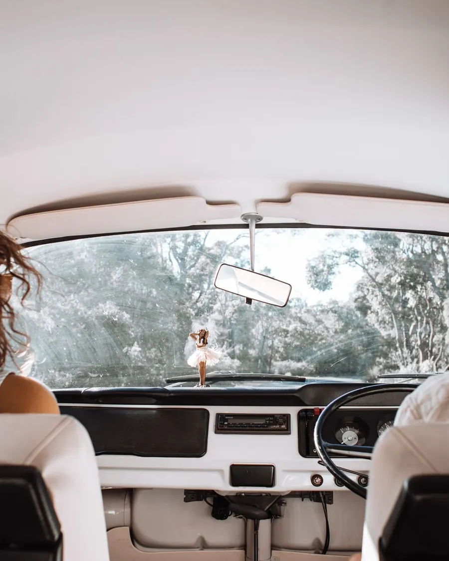 Pareja de espaldas dentro de un auto clásico, viendo el paisaje a través del parabrisas