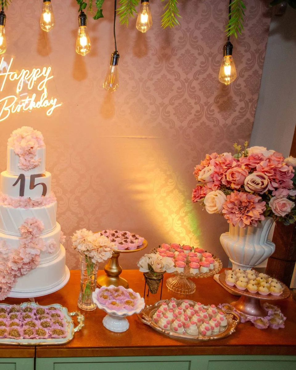 Mesa de postres con el pastel de quince años, flores y dulces