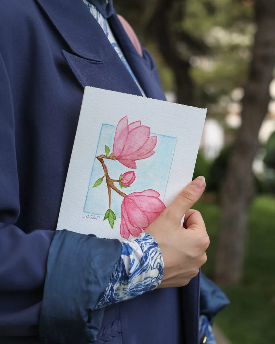 Mano sosteniendo una acuarela floral azul y rosa junto a un blazer navy