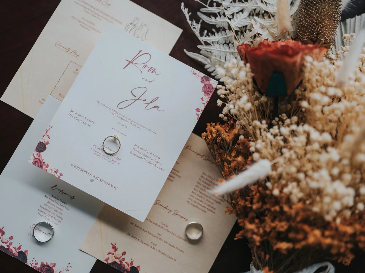Papelería de invitación elegante con flores secas y anillos sobre una mesa