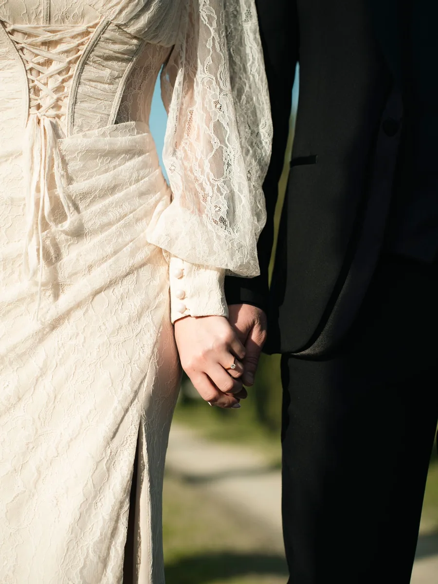 Pareja tomada de la mano vestidos de novios, detalle de encaje y traje